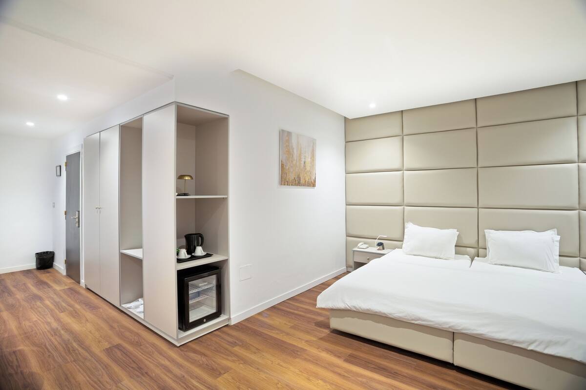 A modern bedroom with a large bed, a wardrobe, a bedside table, and a nightstand.