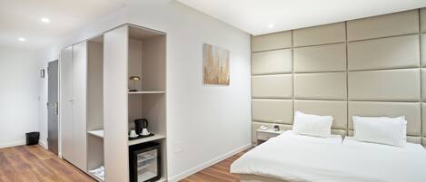 Quarto moderno com cama grande, guarda-roupa, mesa de cabeceira e apoio para objetos.