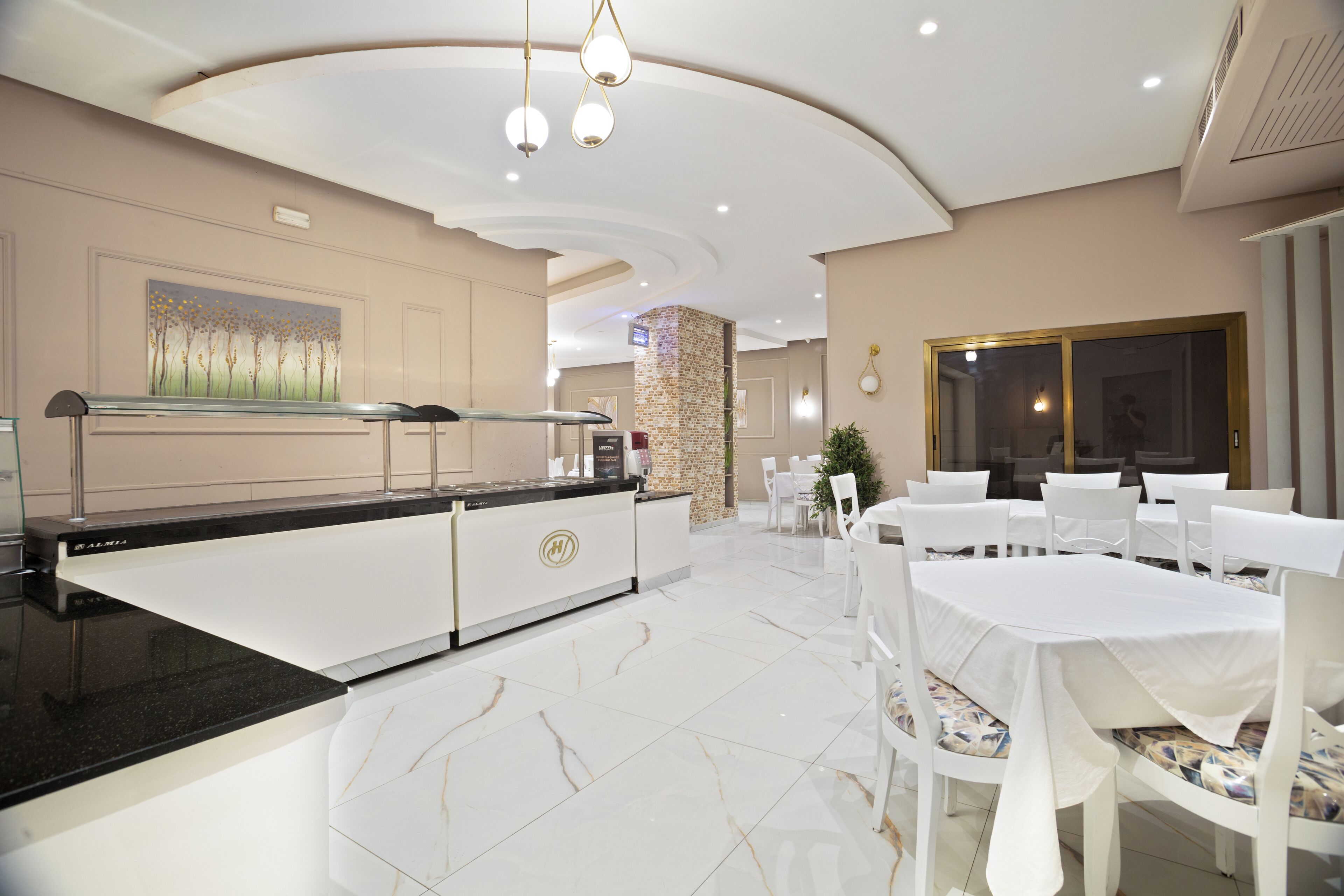 Een moderne hotel lobby met een receptiebalie, witte tafels en stoelen gerangschikt voor eten.