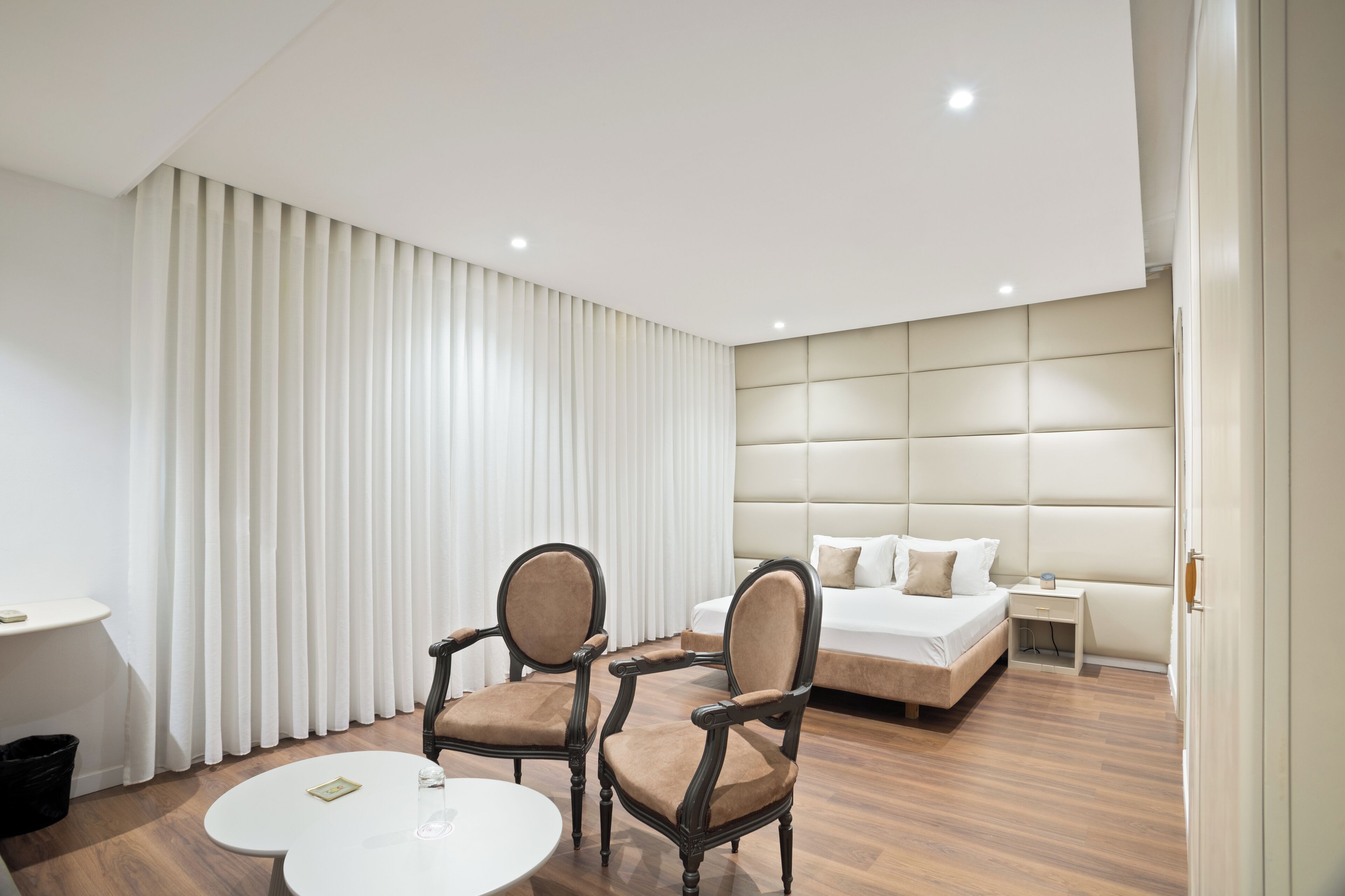 Een moderne hotelkamer met een groot bed, twee fauteuils, een bijzettafeltje en een nachtkastje.