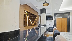 A modern hotel lobby with a long reception desk, a wooden accent wall, a large pillar, and a seating area with a sofa and ottoman. - Hotel Donia Sfax (Sfax Ouest)