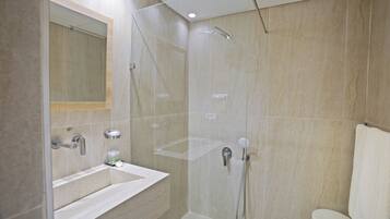 Un baño moderno con ducha de vidrio, un lavamanos con espejo y un inodoro.