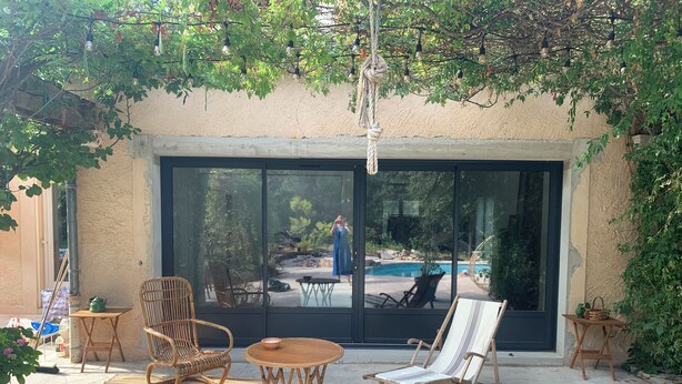 A patio with wicker furniture, a table, and a chair, overlooking a pool and garden.