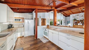Eine moderne Küche mit weißen Schränken, einer Holzbalkendecke und einer großen Kochinsel mit Spüle.