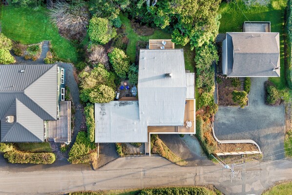 An aerial view of a residential area with a house featuring a large roof, a driveway, and a small garden.