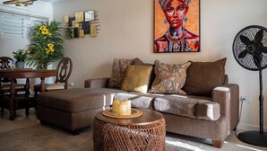 Ein Wohnzimmer mit einer Couch, einem runden Couchtisch, einem Esstisch mit Stühlen und einem Bild an der Wand.