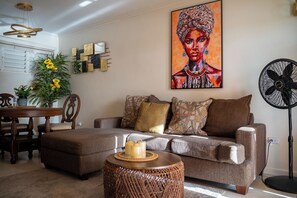 Un salon comprenant un canapé, une table basse ronde, une table à manger avec des chaises et un tableau accroché au mur.