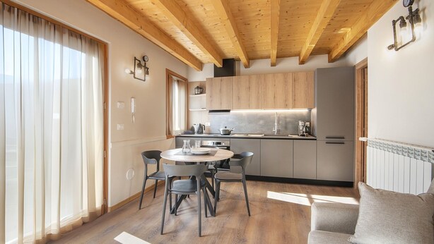 A modern kitchen with wooden beams, a dining area with a round table and chairs, and a built-in oven. - Silia's Home - Two Bedroom Apartment, Sleeps 4 (Vione)