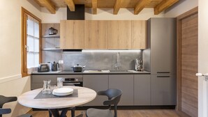 A compact kitchen with wooden cabinets, a stainless steel sink, and a round dining table with chairs. - Silia's Home - Two Bedroom Apartment, Sleeps 4 (Vione)