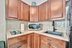 Cocina compacta con armarios de madera, microondas, lavabo y placa de cocina.