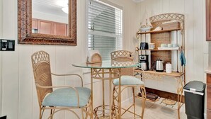 Una cocina compacta con una mesa de vidrio, sillas de mimbre y una estación para café.