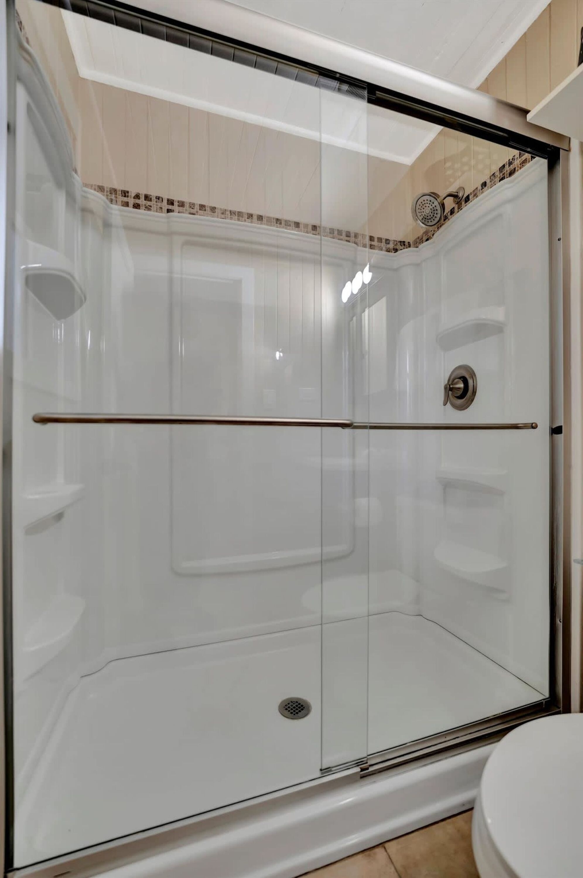 A glass-enclosed shower stall with a white tiled wall, a showerhead, and a control knob.