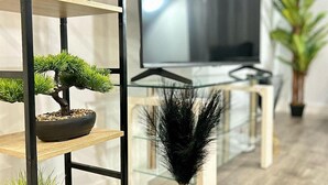 A modern living room with a TV, a bookshelf with a bonsai tree, and a decorative feather arrangement. - 2br-sleeps4-citycentre-parking-rooftop (Birmingham)