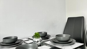 A dining table with a set of grey bowls and plates, a small glass vase with a plant, and a black leather chair. - 2br-sleeps4-citycentre-parking-rooftop (Birmingham)
