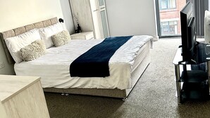 A hotel room with a bed, a TV, and a window with a view of a building. - 2br-sleeps4-citycentre-parking-rooftop (Birmingham)