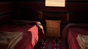 A room with two beds, a wooden nightstand, and a window with a desert view. - Wadi Rum Magic Nature Camp (Wadi Rum)