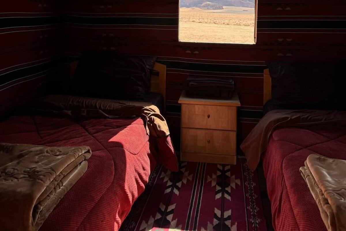 Una habitación con dos camas, una mesita de noche de madera y una ventana con vistas al desierto.