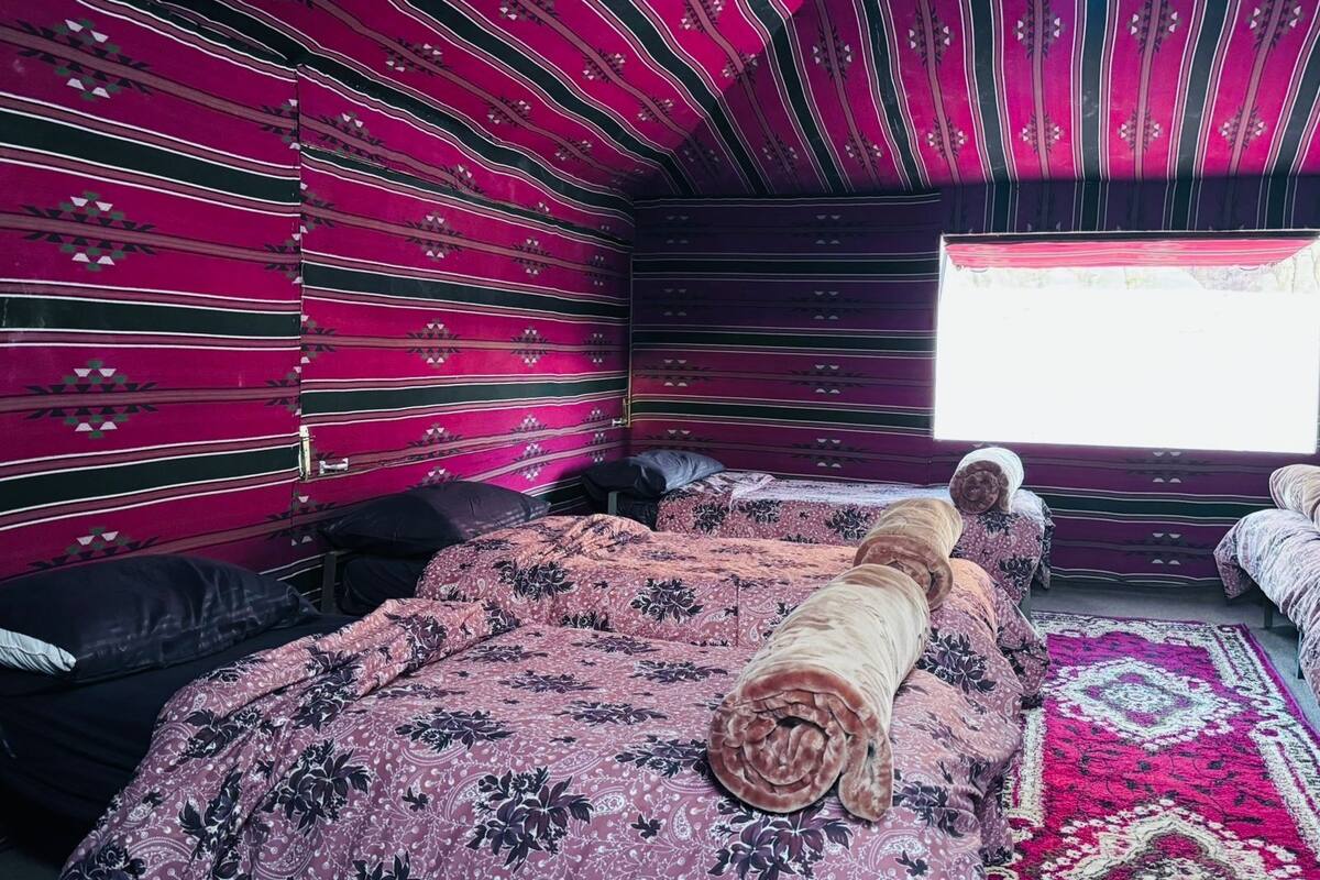 Una habitación con una cama, un edredón enrollado y una ventana con luz natural.