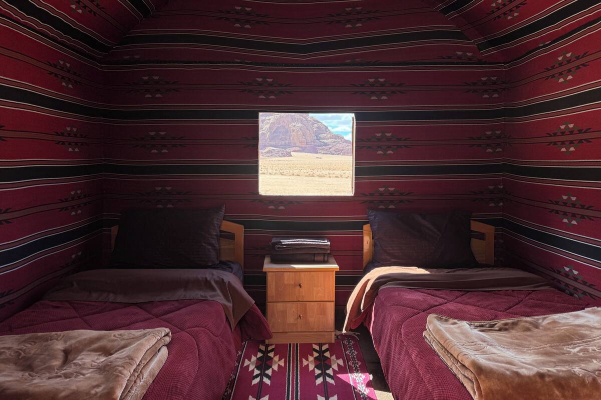 Una habitación con dos camas, una mesita de noche de madera y una ventana con vistas al desierto.