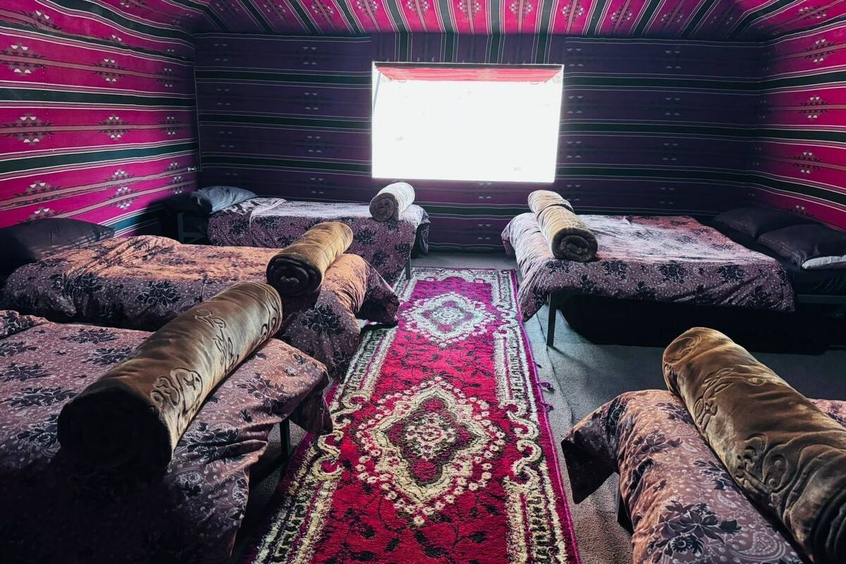 Una habitación con cuatro camas, un ventanal grande y una alfombra estampada.
