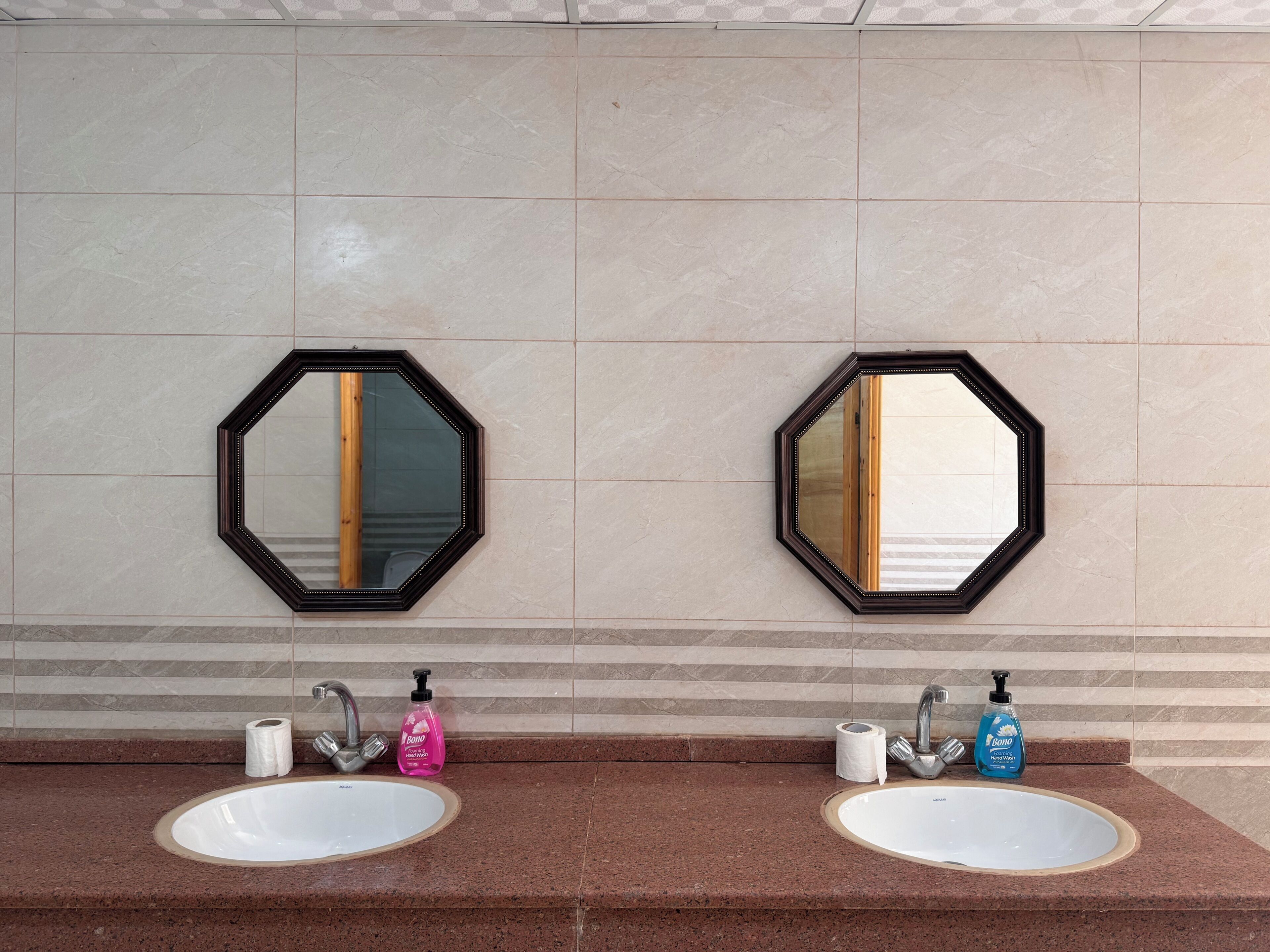 A bathroom with two sinks, each with a mirror above. There are toiletries and paper towels on the counter.
