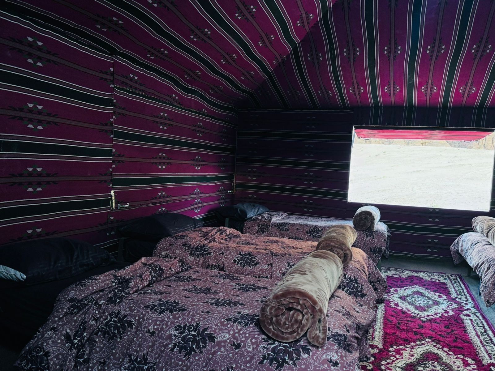 A room with a patterned bedspread, a window with a view, and a patterned rug.