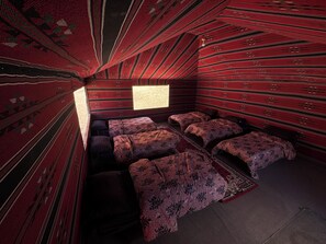 A room with a unique sloped ceiling design, multiple beds with patterned bedding, and a small window providing natural light.