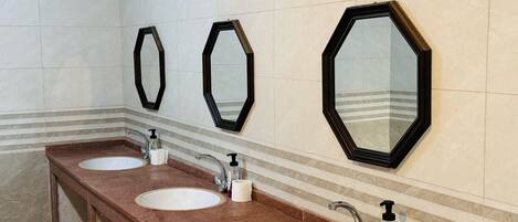 A bathroom with three sinks, each with a mirror above. The walls are tiled, and there are striped lines near the base of the mirrors.