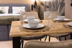 A dining table set with white bowls and wine glasses, placed in a cozy room with a sofa and a bed in the background. - BaliApartment, kitchen, parking lot, 24h digital check-in, Wlan 150MBit (Hof)