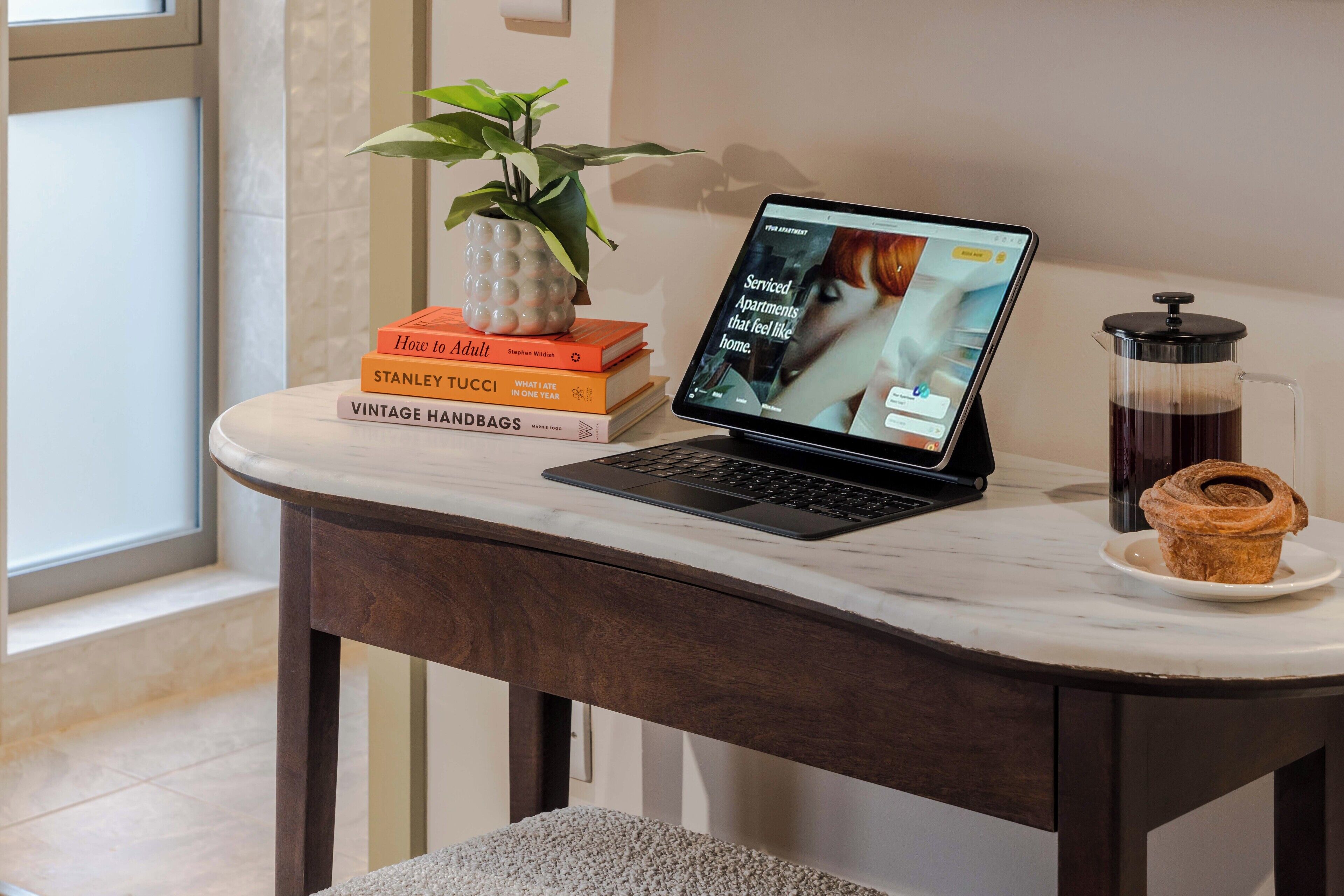 Una laptop sobre una mesa de mármol con una cafetera y un muffin en un plato.