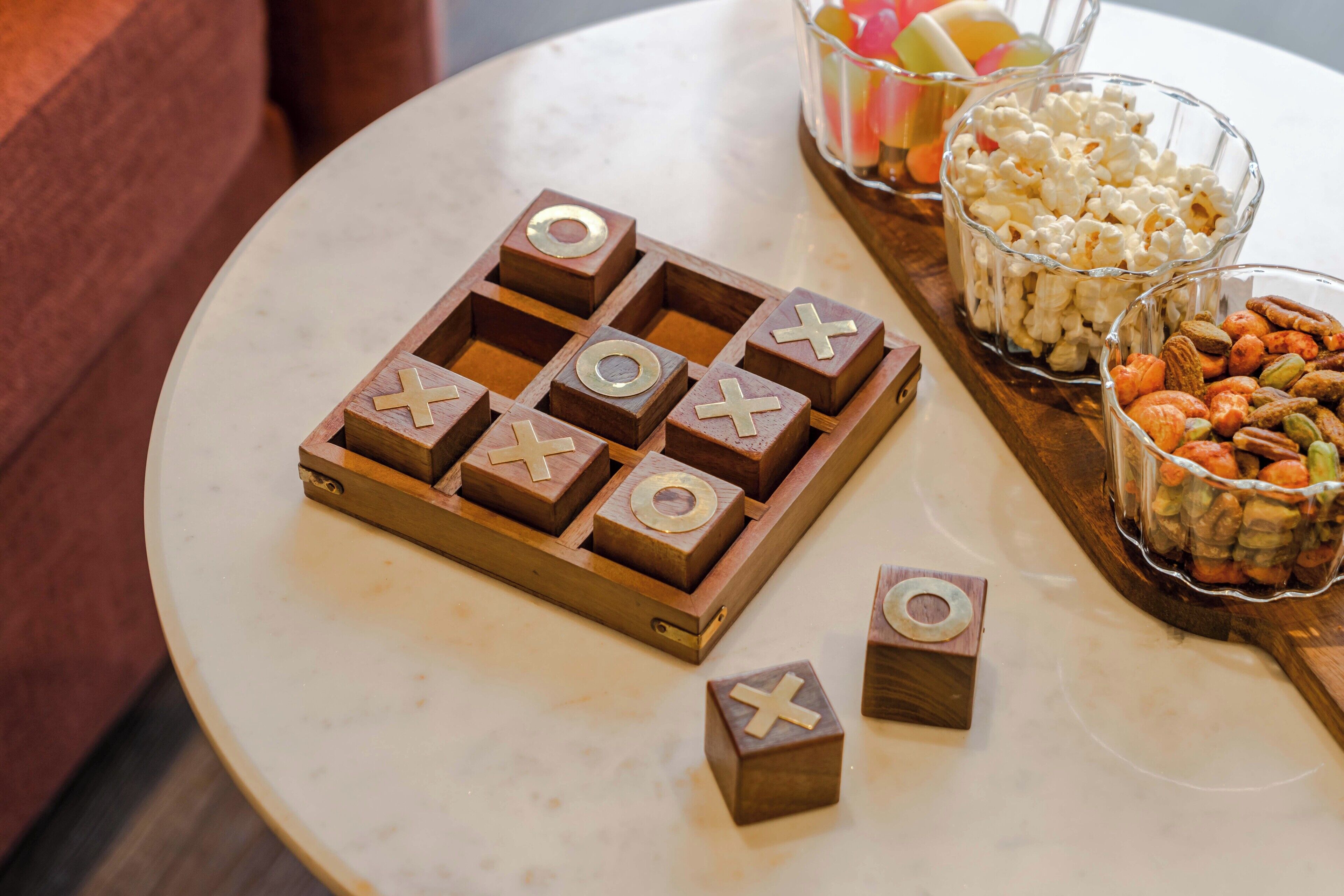 Un juego de tres en raya de madera sobre una mesa redonda, con aperitivos y palomitas.