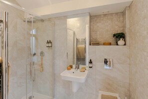 A modern bathroom with a glass-enclosed shower, a sink with toiletries, and a mirror. - Waterside Living I Luxe Apartments (Bristol)