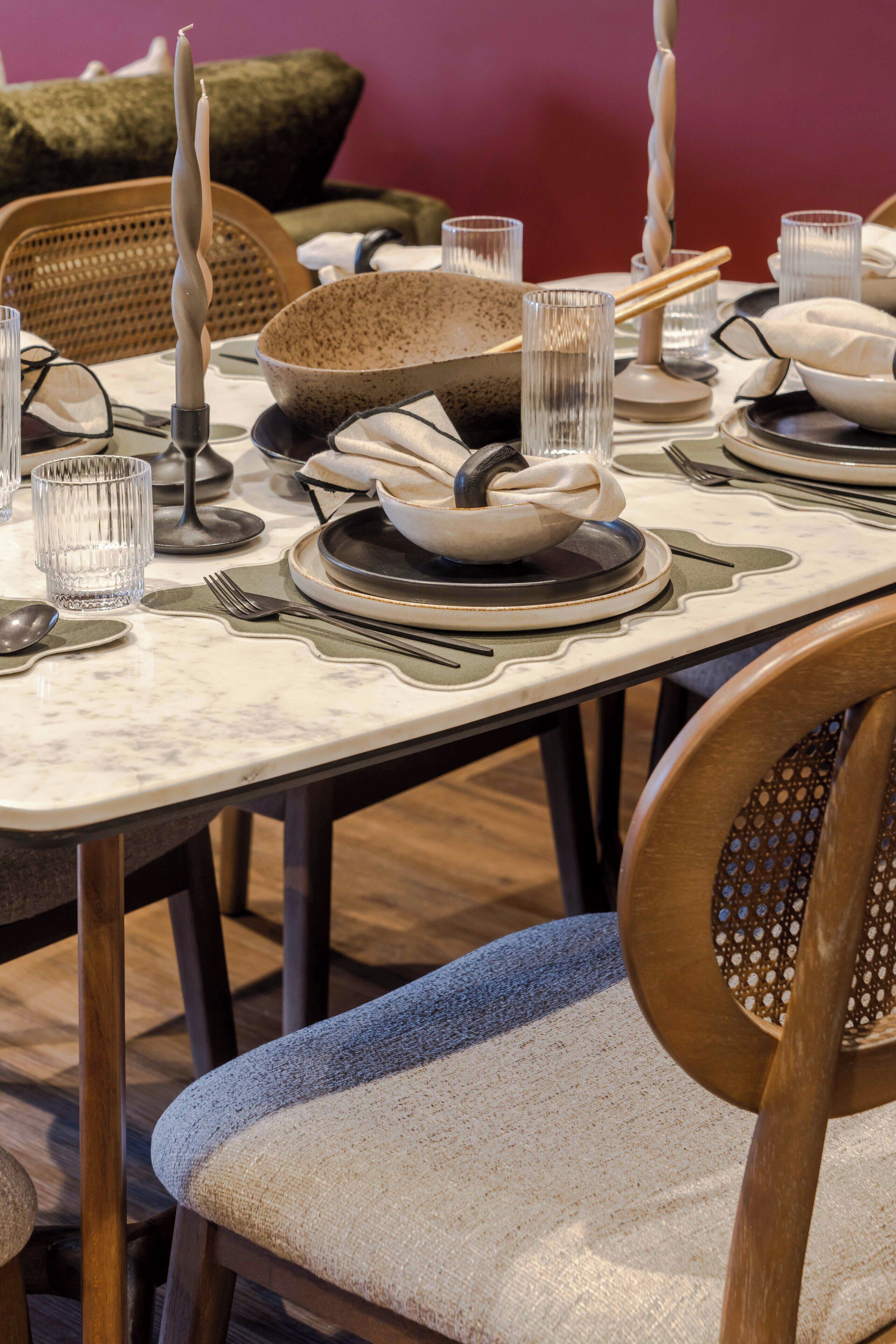 Une table à manger dressée avec des assiettes, des bols, des verres et des couverts, avec une chaise au premier plan.