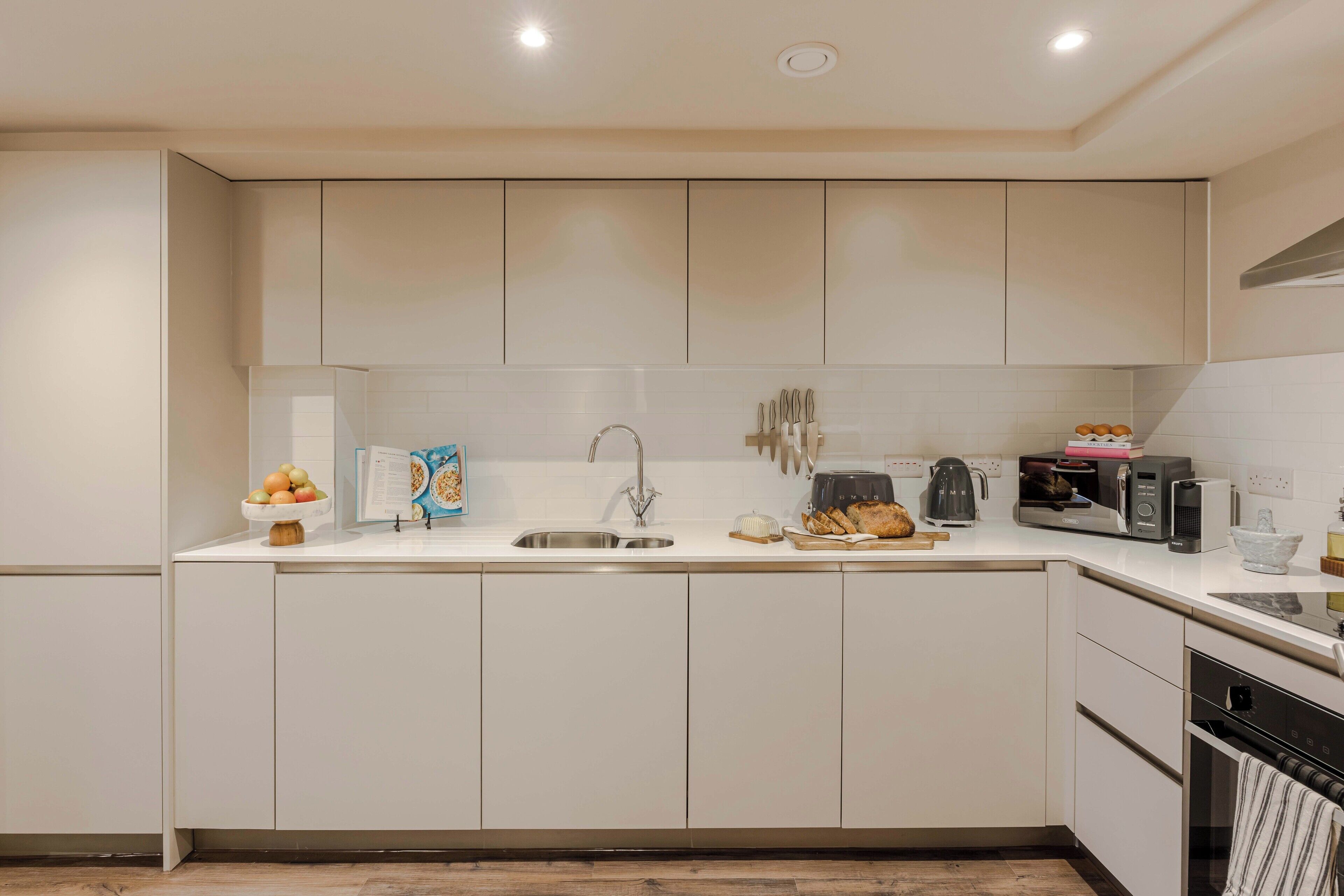 A modern kitchen with white cabinets, a stainless steel sink, and a built-in oven.