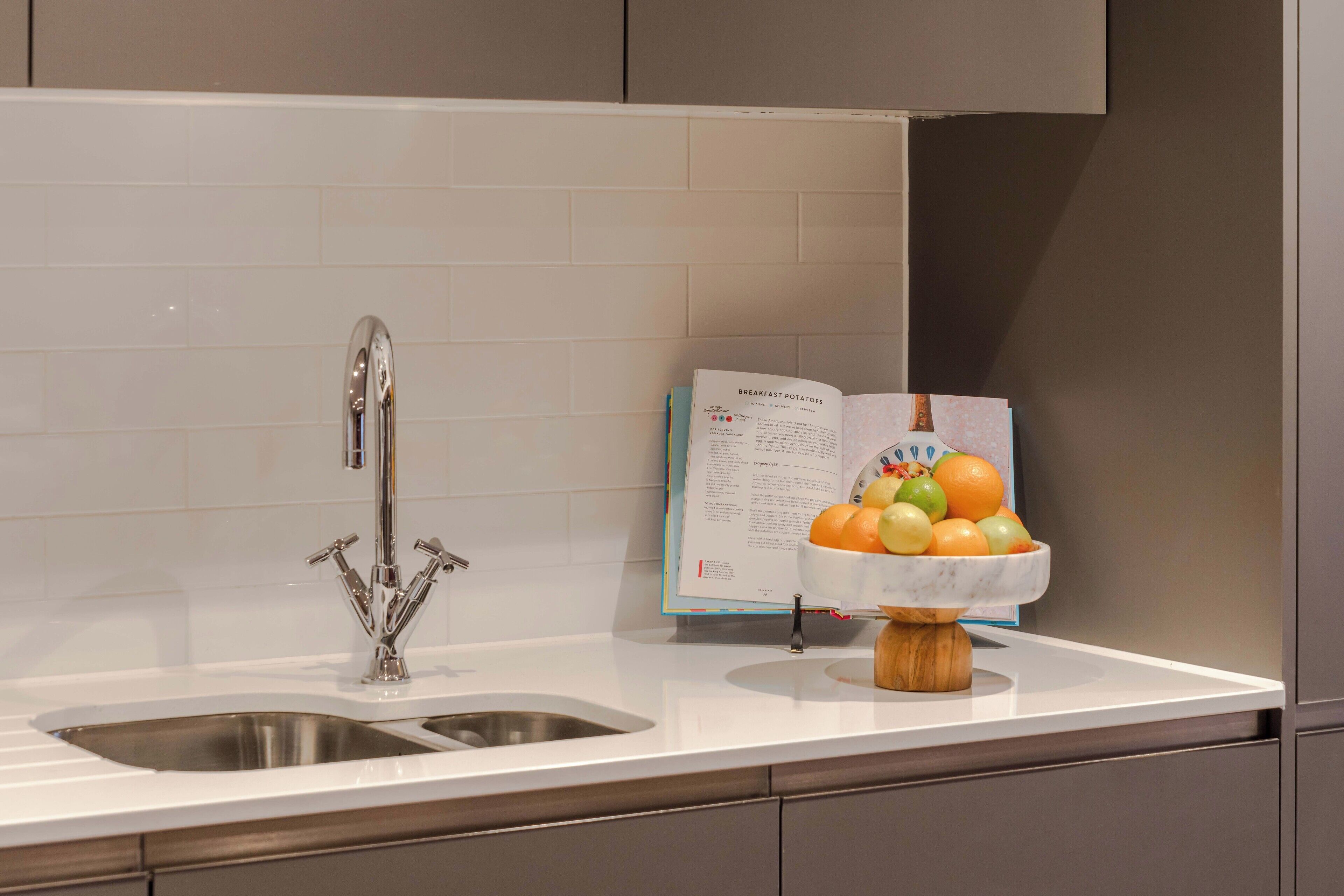 A kitchen with a stainless steel sink, a marble countertop, and a bowl of fruit.