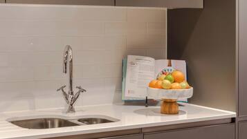 A kitchen with a stainless steel sink, a marble countertop, and a bowl of fruit.