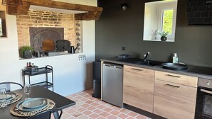 Una cocina compacta con pared de piedra, vigas de madera, horno empotrado, lavamanos y lavavajillas.