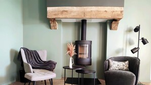 Una sala de estar acogedora con una chimenea moderna, dos sillones, una mesita y una lámpara de pie.