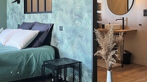 Un dormitorio moderno con una cama, una mesita, un espejo y un florero con plantas secas.