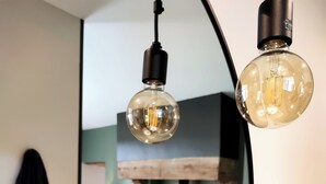 Una sala de estar moderna con chimenea, un espejo redondo que refleja la estancia, y dos lámparas colgantes.