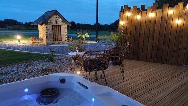 Una terraza de madera con un jacuzzi, sillas de mimbre y un edificio de piedra al fondo.