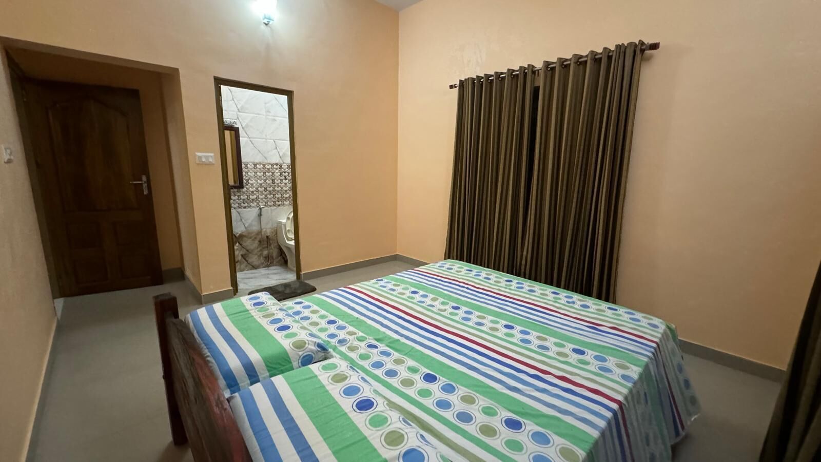 Une chambre avec un lit, une porte en bois, une salle de bain visible à travers une porte en verre et un radiateur.