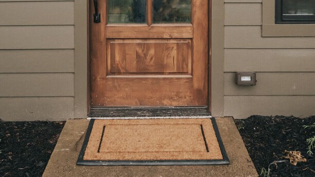 Puerta de madera con panel de vidrio, buzón y aplique de luz exterior.