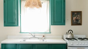 A kitchen with teal cabinets, a white sink, a gas stove, and a lace window shade.