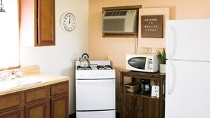 A kitchen with a stove, microwave, and refrigerator. There is a clock on the wall and a welcome sign. - Cabin #2 at Beaver Creek (Strasburg)