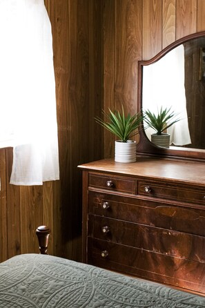 Une commode en bois avec un miroir, deux plantes en pot et un tapis à motifs.