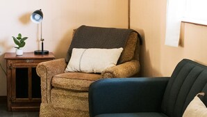 A cozy living room with a brown armchair, a blue sofa, a small wooden side table with a lamp, and a framed picture on the wall. - Cabin #2 at Beaver Creek (Strasburg)