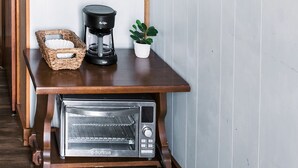 Una mesa de madera con una cafetera, un tostador, una cesta y un reloj en la pared.