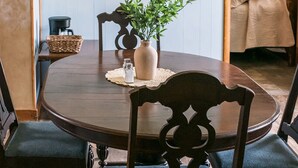 Un comedor con una mesa redonda, cuatro sillas, un florero con plantas verdes, una cafetera y un salero.