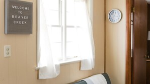 Una habitación con una cama, una ventana con cortinas blancas, un reloj y un cartel de bienvenida en la pared.